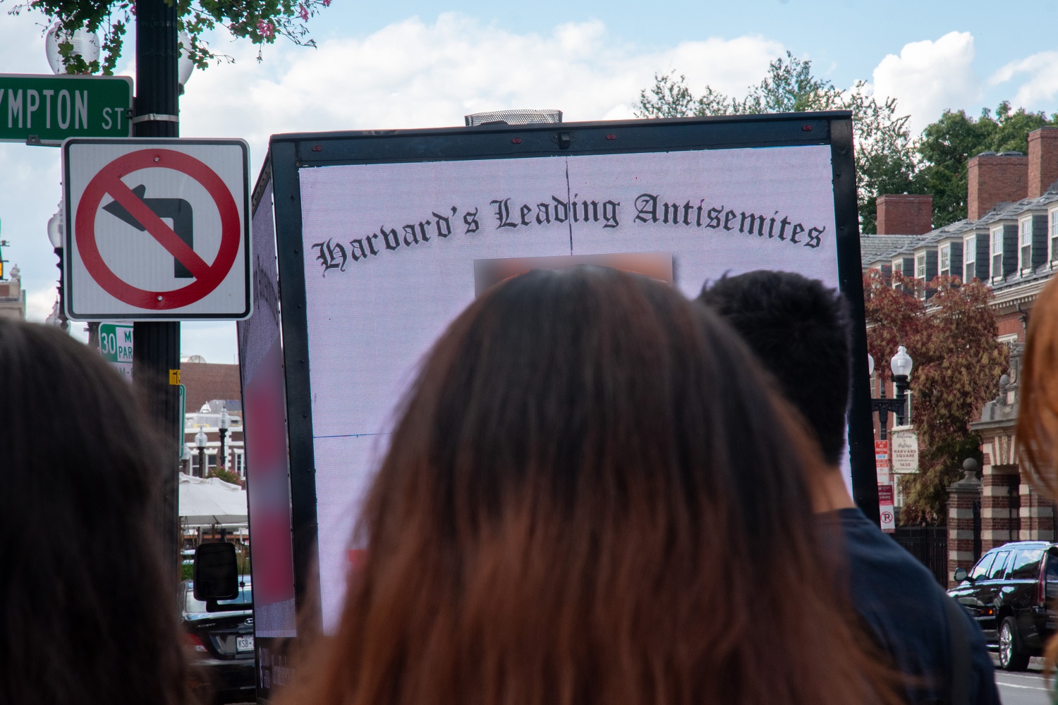 Passers-by observe the billboard truck displaying students’ faces and names Thursday. The Crimson blurred parts of this photograph to avoid identifying students due to retaliation concerns.